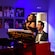 Performer in an elegant gown singing beside a pianist in formal attire, with portraits and vibrant lighting